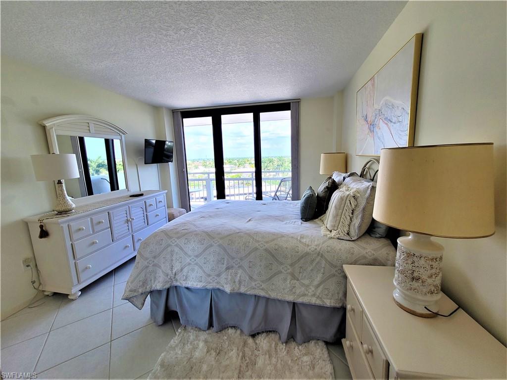 Bedroom featuring a textured ceiling, access to outside, light tile patterned floors, and floor to ceiling windows