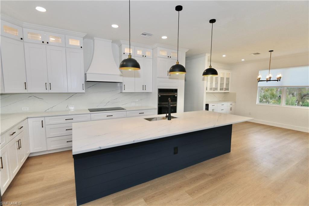 Kitchen featuring glass insert cabinets, light stone countertops, white cabinets, custom range hood, and a center island with sink