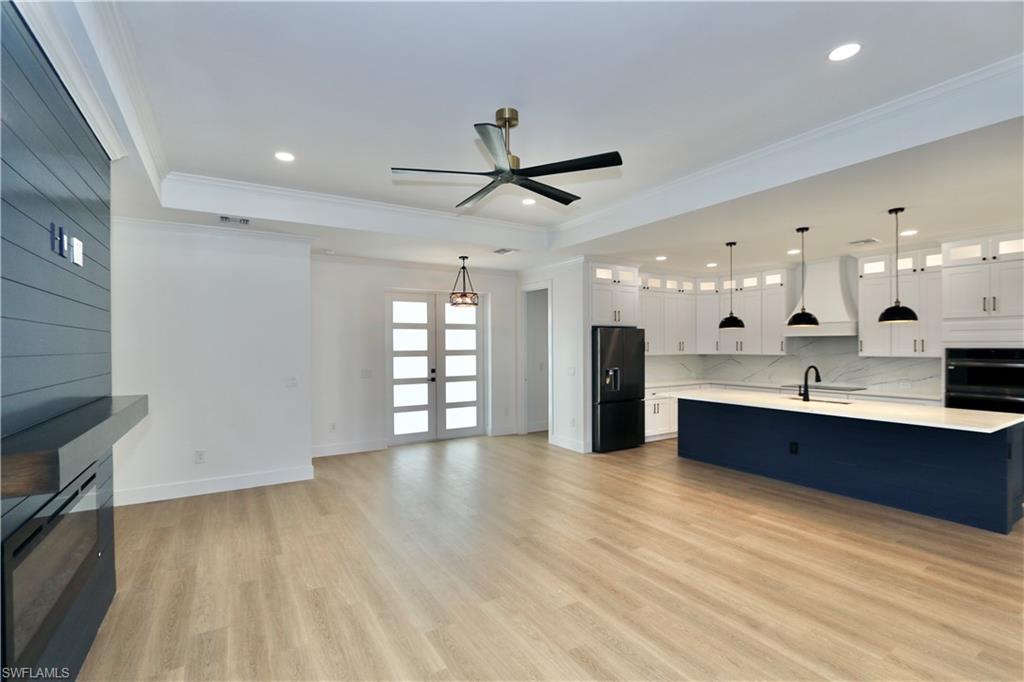 Unfurnished living room with a tray ceiling, crown molding, light wood-style flooring, a fireplace, and ceiling fan