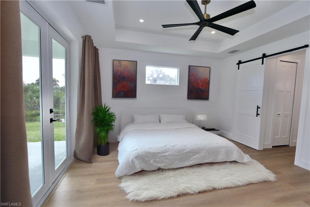 Virtually Staged Primary Bedroom with a barn door, a tray ceiling, access to exterior, light wood-style flooring, and recessed lighting