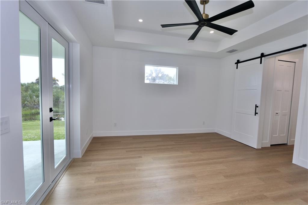 Primary Bedroom with a barn door, a tray ceiling, access to exterior, light wood-style flooring, and recessed lighting