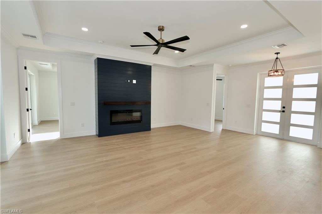 Unfurnished living room with a tray ceiling, crown molding, light wood-style flooring, a fireplace, and ceiling fan