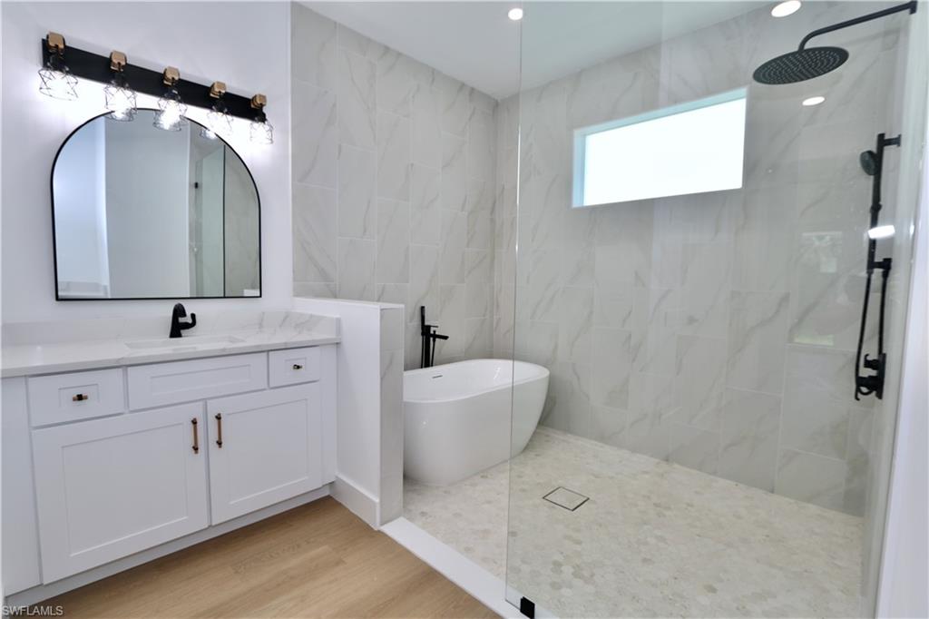 Primary bathroom featuring a marble finish wet room shower, vanity, a freestanding bath, light wood-style flooring, and tile walls