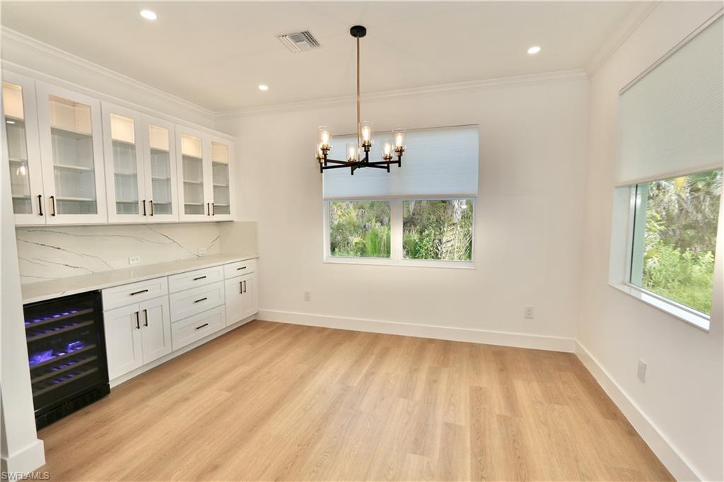Dry Bar featuring glass insert cabinets, hanging light fixtures, healthy amount of natural light, beverage cooler, and ornamental molding