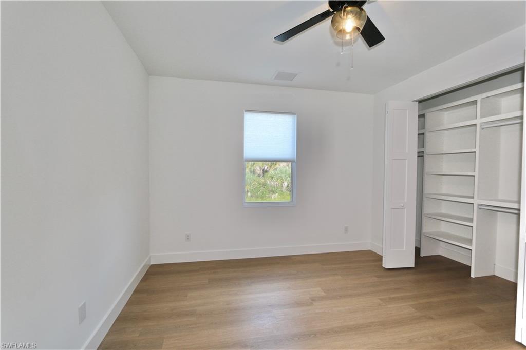 Unfurnished bedroom featuring light wood finished floors, a closet with custom wood closet organizer system and a ceiling fan
