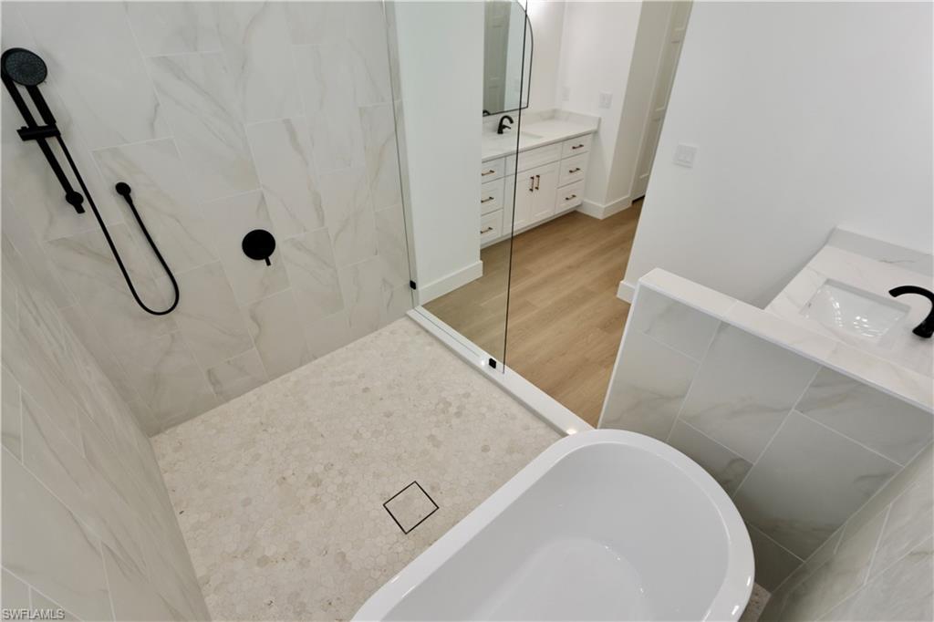 Primary bathroom featuring a marble finish wet room shower, vanity, a freestanding bath, light wood-style flooring, and tile walls