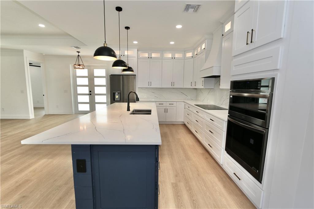 Kitchen featuring decorative backsplash, light wood-style floors, white cabinets, glass insert cabinets, and hanging light fixtures