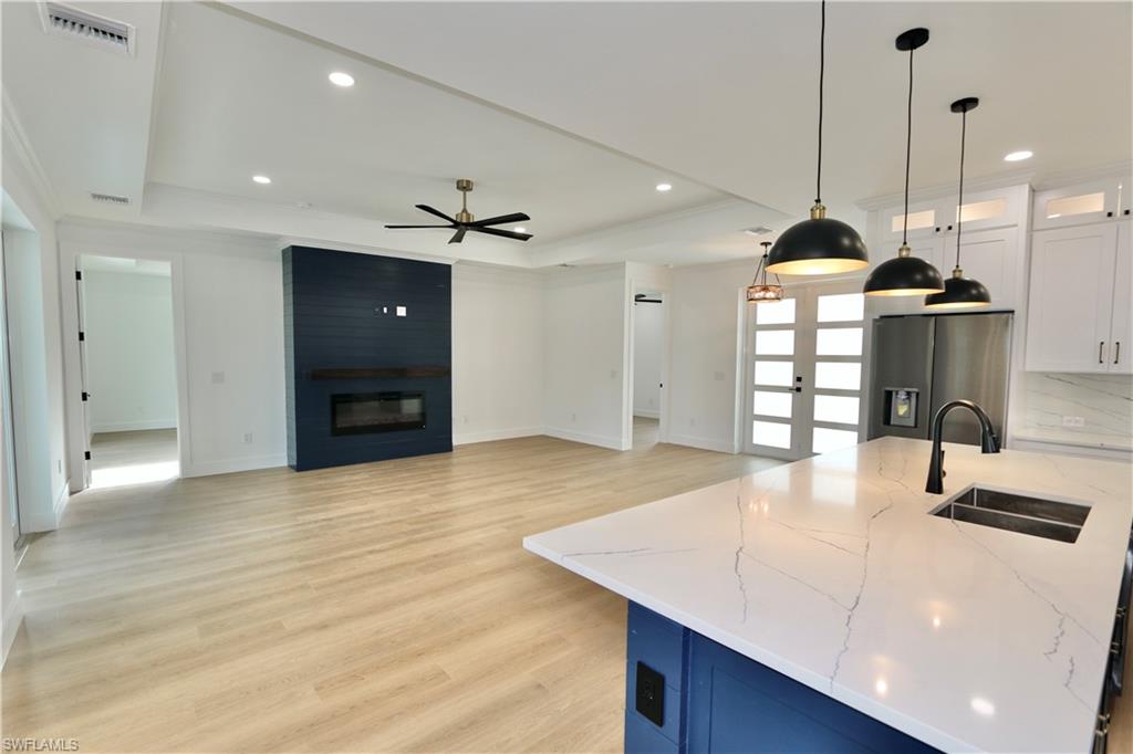 Kitchen with a tray ceiling, an island with sink, light wood finished floors, pendant lighting, and white cabinets