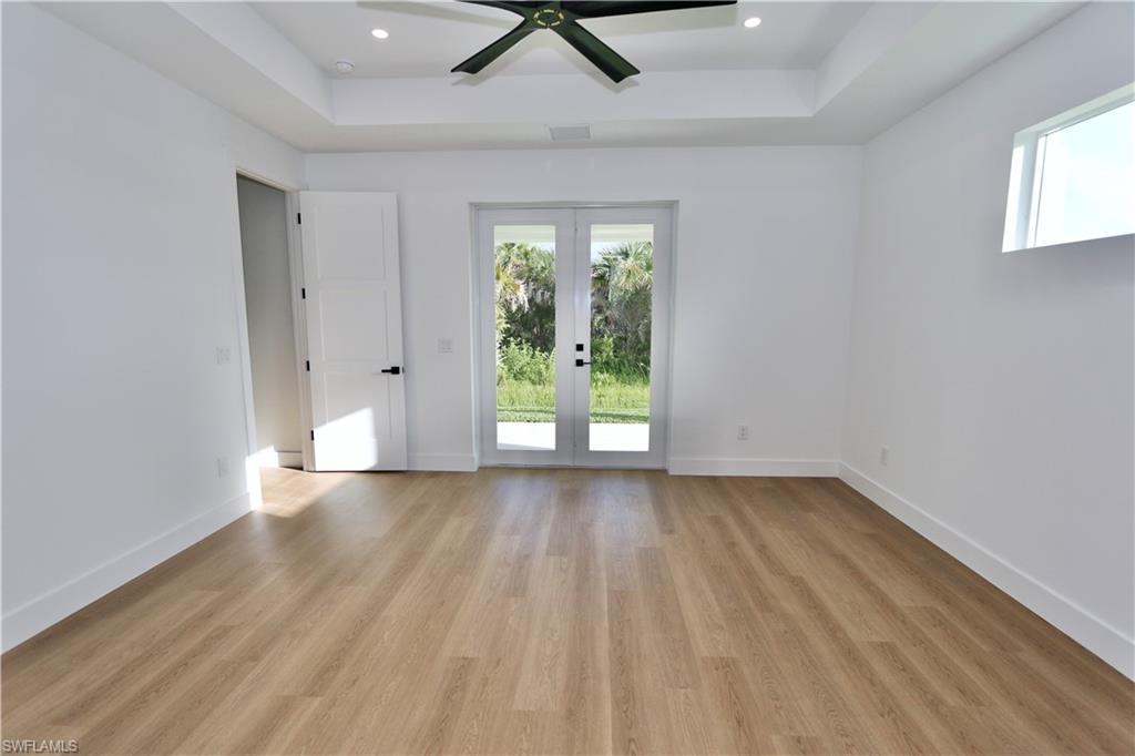 Primary Bedroom with a barn door, a tray ceiling, access to exterior, light wood-style flooring, and recessed lighting