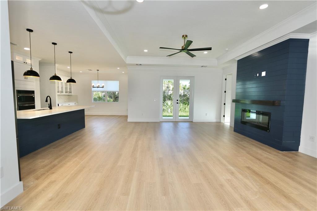 Unfurnished living room featuring a raised ceiling, a large fireplace, a chandelier, light wood finished floors, and recessed lighting