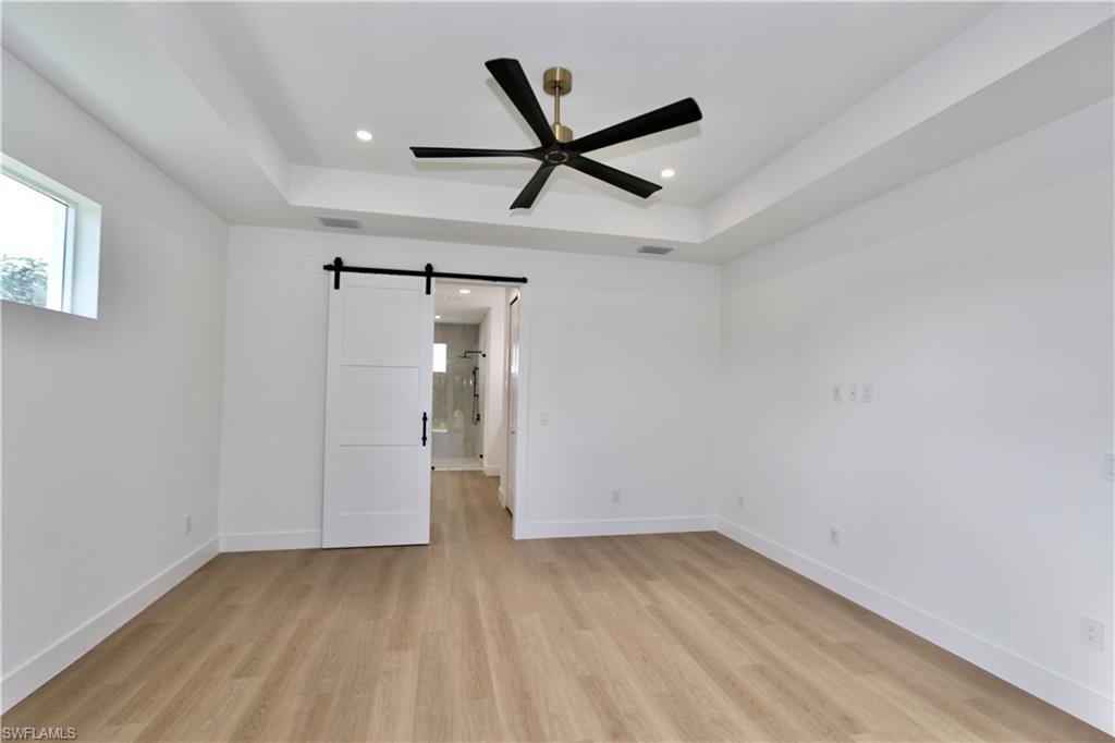 Primary Bedroom with a barn door, a tray ceiling, access to exterior, light wood-style flooring, and recessed lighting