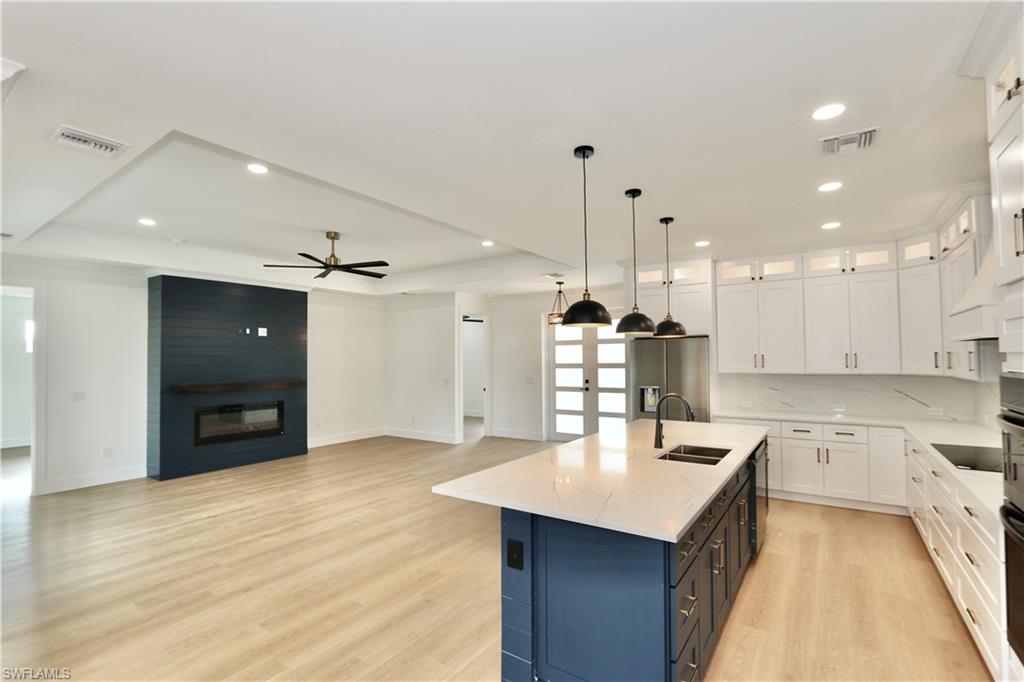 Kitchen with white cabinets, light wood finished floors, a raised ceiling, decorative light fixtures, and recessed lighting