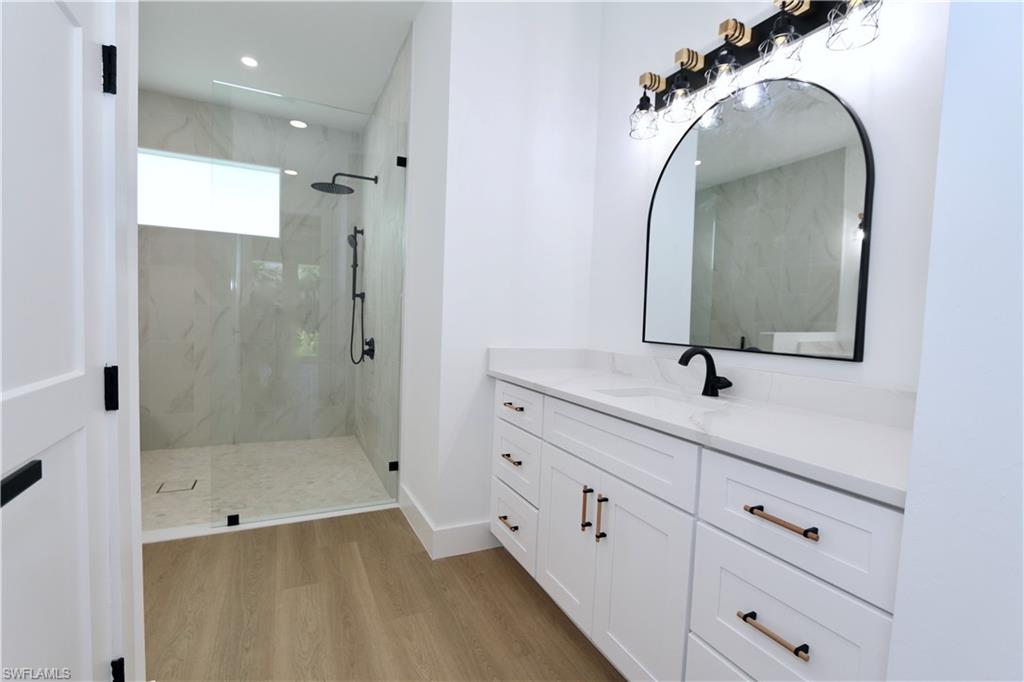 Primary bathroom featuring a marble finish wet room shower, vanity, a freestanding bath, light wood-style flooring, and tile walls