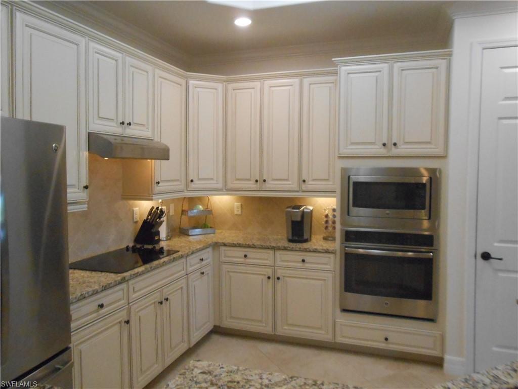 Kitchen with stainless steel appliances, light stone counters, under cabinet range hood, and light tile patterned floors