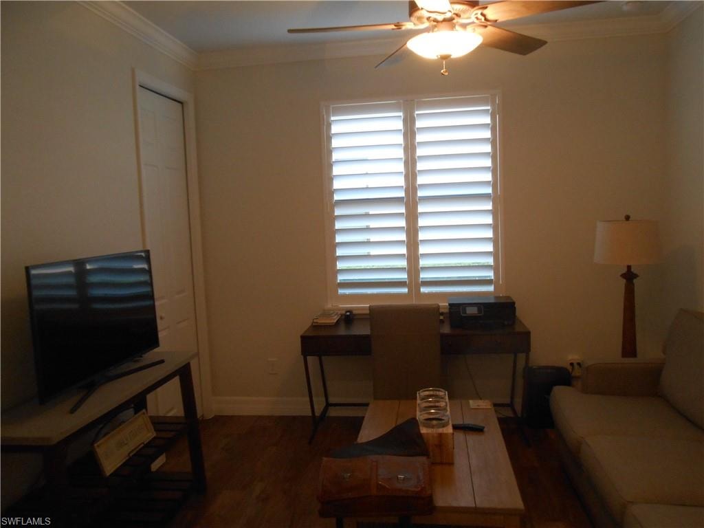 Living room with crown molding, dark wood-style flooring, and a ceiling fan