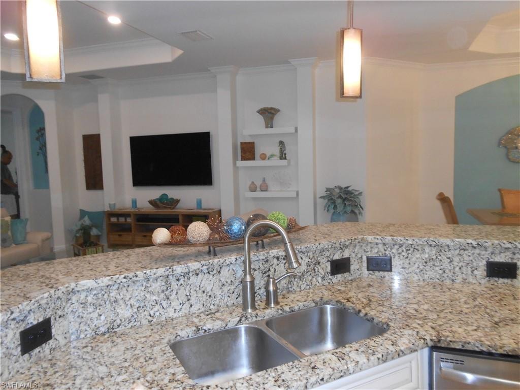Kitchen featuring crown molding, arched walkways, light stone countertops, decorative light fixtures, and a raised ceiling