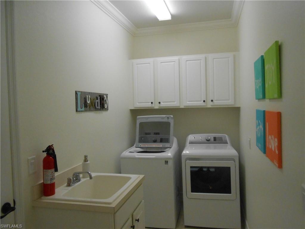 Laundry area featuring ornamental molding, washing machine and clothes dryer, and cabinet space