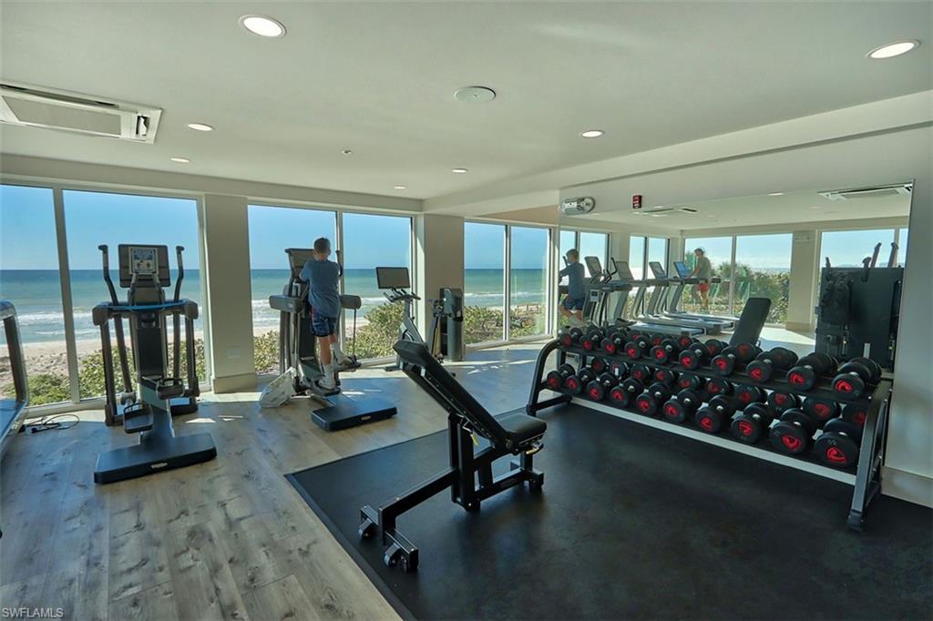 Gym featuring recessed lighting, view of water and beach, and wood finished floors