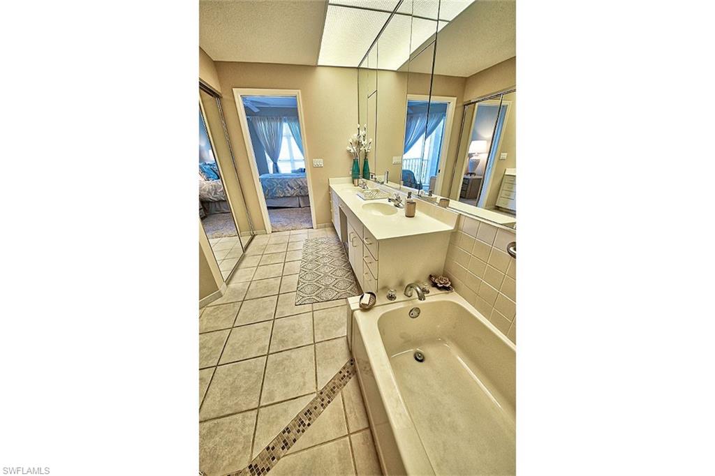 Full bathroom with ensuite bath, light tile patterned floors, a bath, double vanity, and a textured ceiling