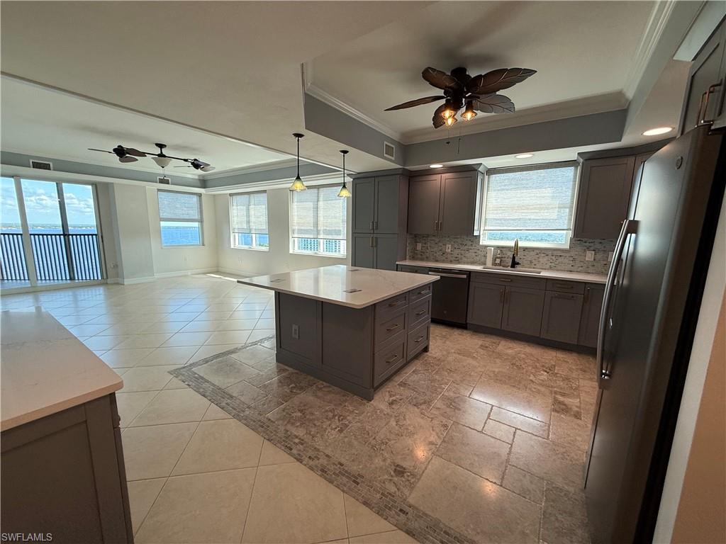 Kitchen featuring freestanding refrigerator, ornamental molding, a raised ceiling, a ceiling fan, and open floor plan