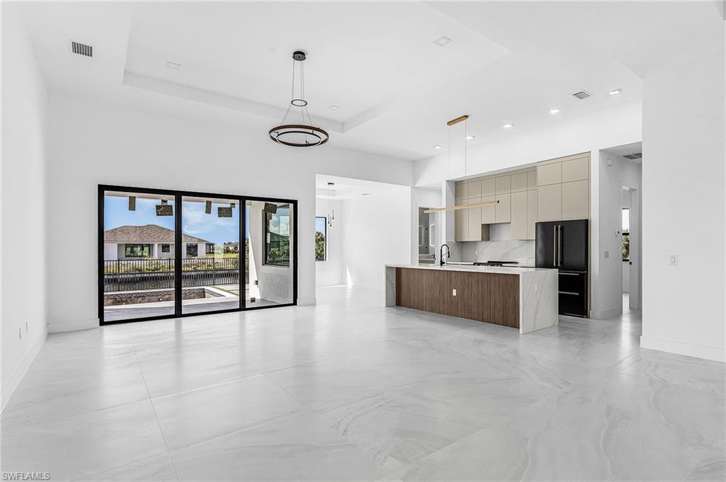 Kitchen with modern cabinets, decorative light fixtures, a tray ceiling, high quality fridge, and open floor plan
