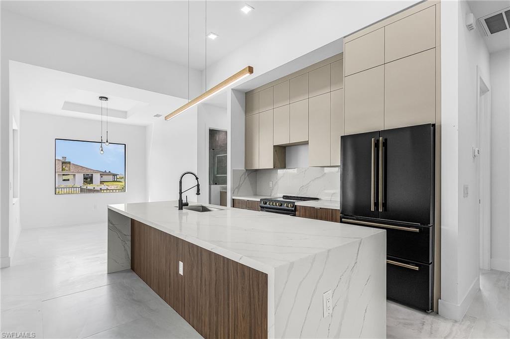 Kitchen with cream cabinetry, modern cabinets, high end black fridge, backsplash, and decorative light fixtures