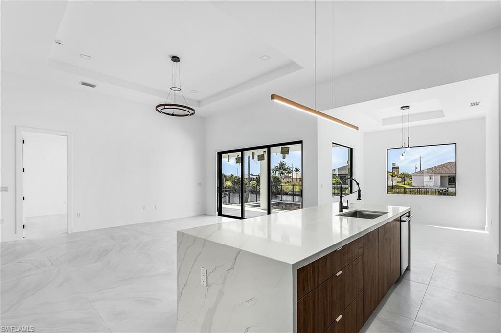Kitchen with a raised ceiling, modern cabinets, decorative light fixtures, dark brown cabinets, and open floor plan