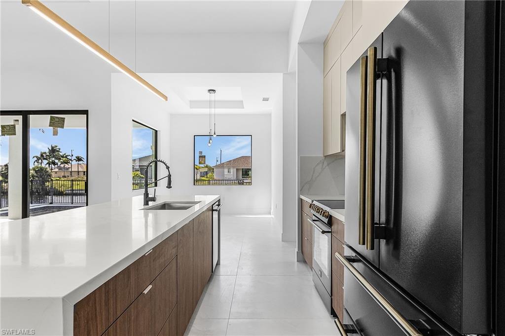 Kitchen with freestanding refrigerator, light stone counters, range with electric stovetop, decorative light fixtures, and a spacious island