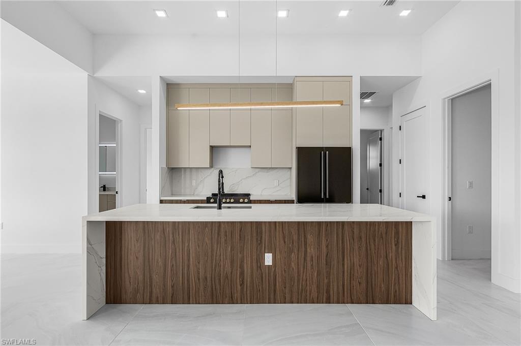 Kitchen with modern cabinets, light stone countertops, decorative backsplash, built in fridge, and recessed lighting