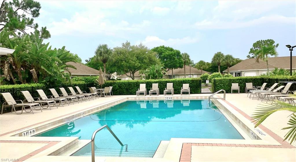 Community swimming pool featuring a concrete deck with brick-patterned accents, multiple lounge chairs, and a black metal perimeter fence