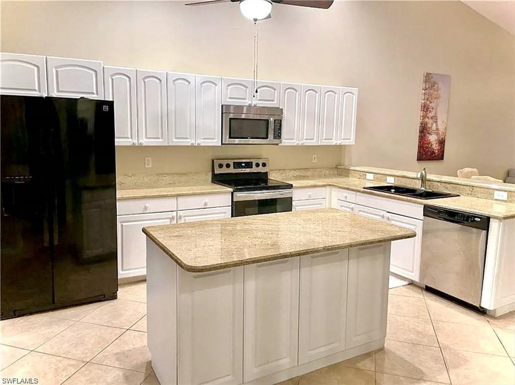 Kitchen featuring an island, white cabinetry, integrated stainless steel appliances, light-toned countertops, and tile flooring