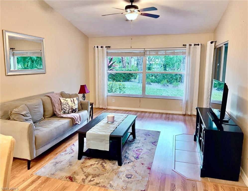 Living area featuring large windows, wood-finish flooring, and a ceiling fan