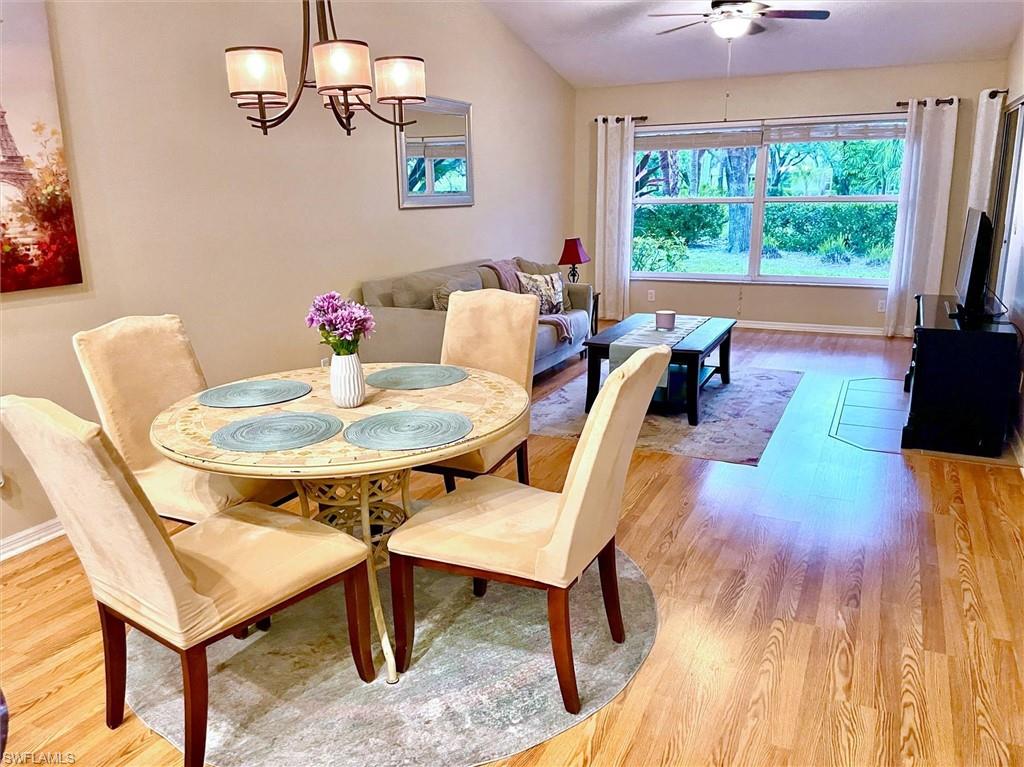 Open-concept living and dining area featuring wood-finish flooring, a vaulted ceiling, a large picture window, and a ceiling fan