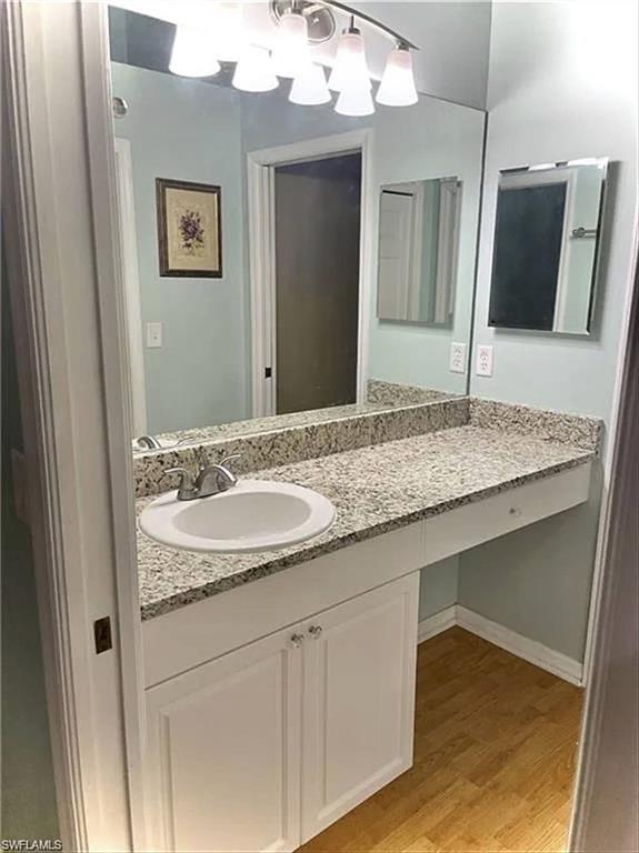 Bathroom vanity featuring a speckled countertop, integrated sink with chrome faucet, full-width mirror, and wood-finish flooring