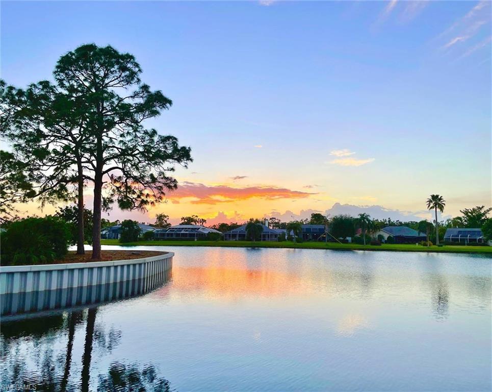 Waterfront property featuring a curved sea wall, mature trees, and landscaping