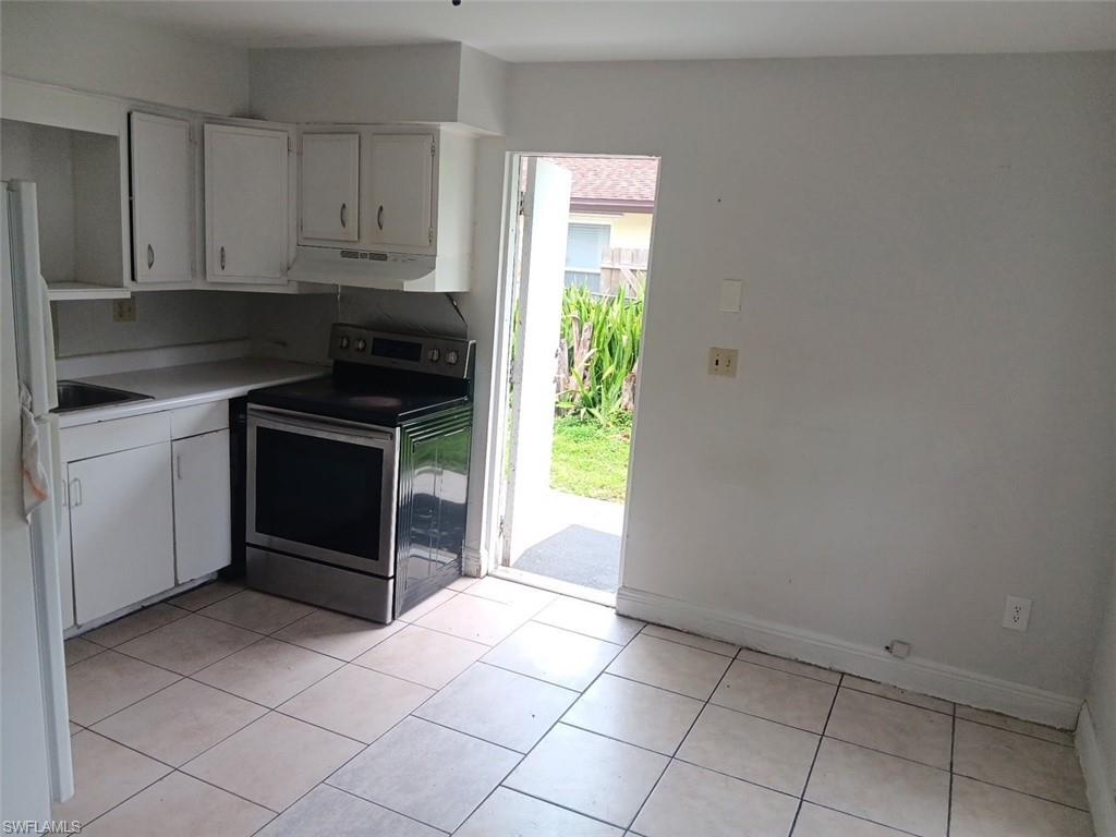 Kitchen with white cabinets, stainless steel electric range, light tile patterned floors, and freestanding refrigerator