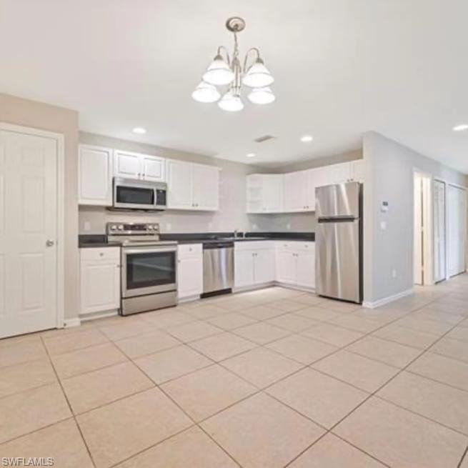 Kitchen with white cabinets, appliances with stainless steel finishes, hanging light fixtures, light tile patterned floors, and dark countertops