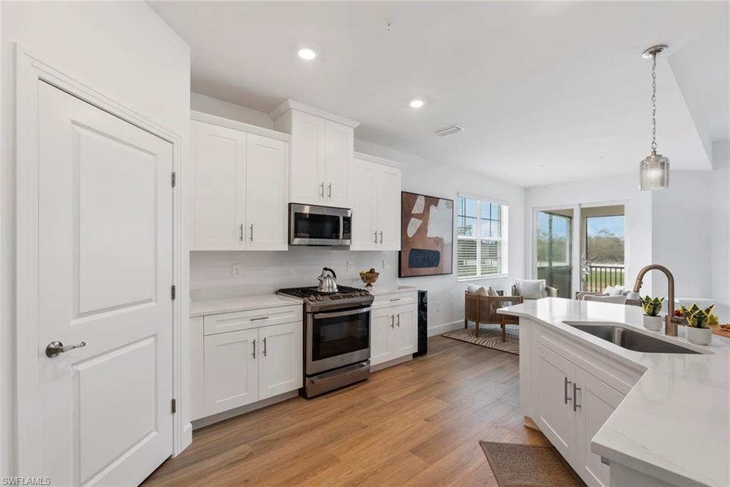 Kitchen featuring white cabinetry, sink, stainless steel appliances, decorative light fixtures, and light wood-type flooring