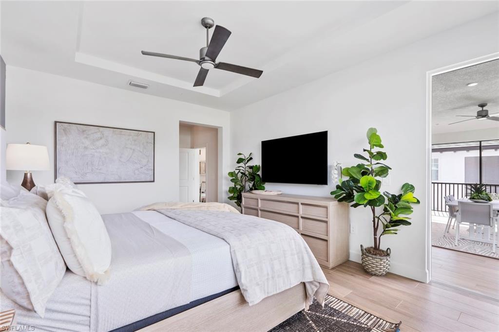 Bedroom with light hardwood / wood-style floors, ceiling fan, and a tray ceiling