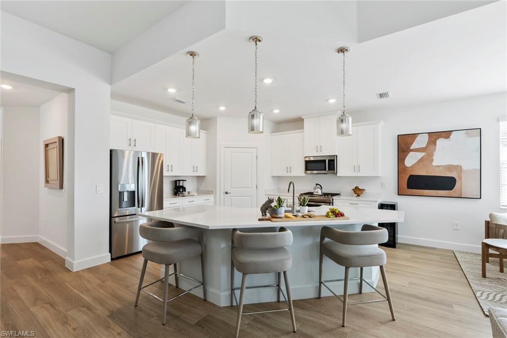Kitchen featuring hanging light fixtures, stainless steel appliances, light hardwood / wood-style flooring, an island with sink, and white cabinets