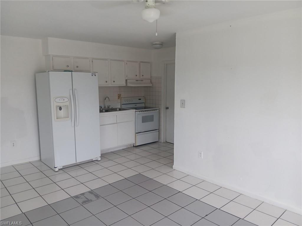 Kitchen featuring white appliances, decorative backsplash, light countertops, under cabinet range hood, and light tile patterned floors
