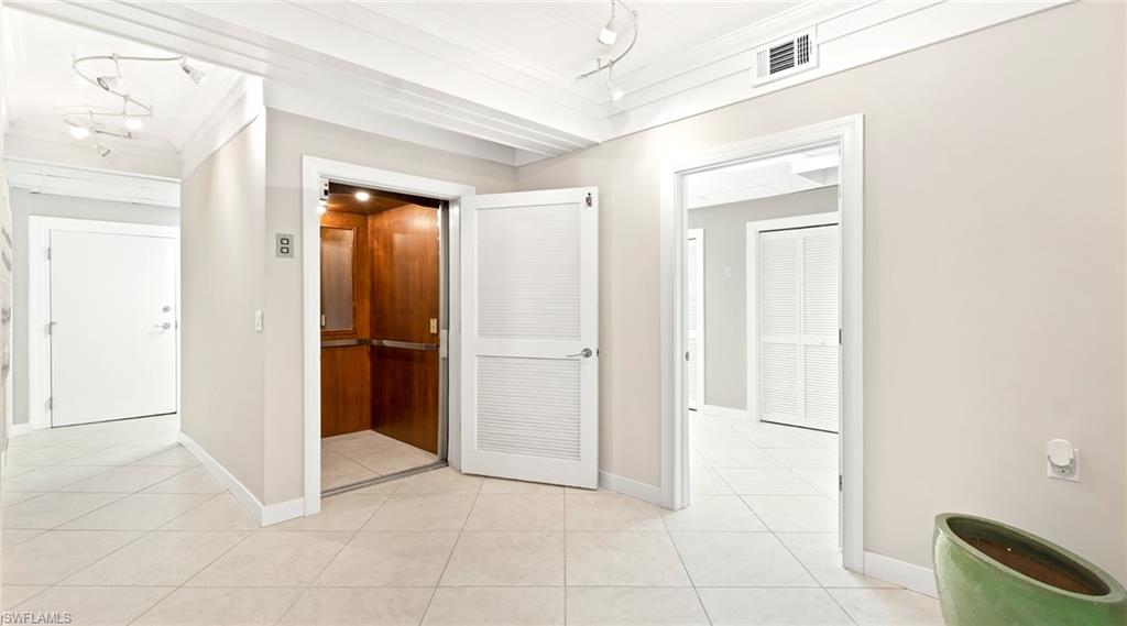 Hallway featuring elevator, ornamental molding, light tile patterned floors, and track lighting