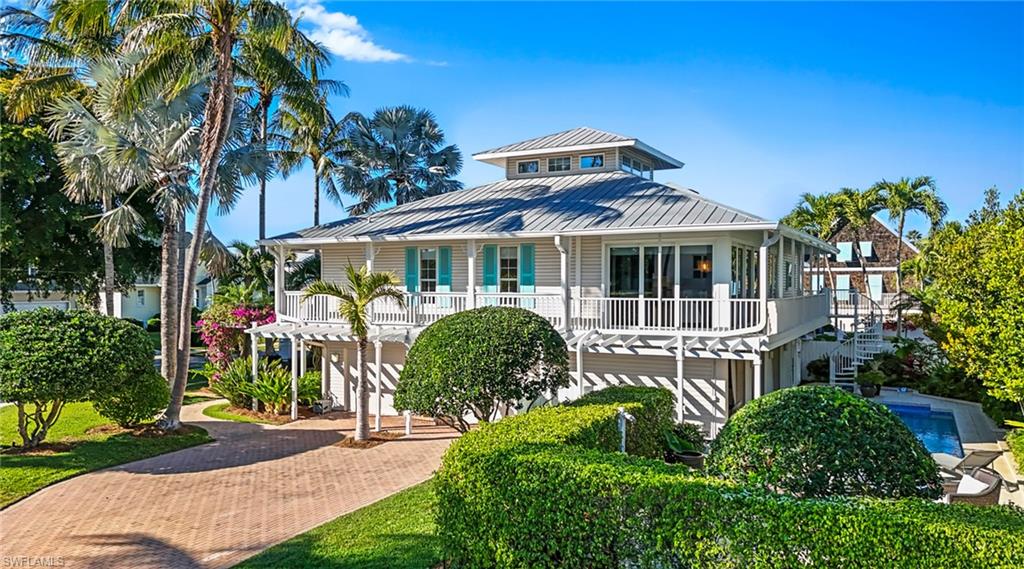 Coastal inspired home with decorative driveway, a standing seam roof, and a balcony