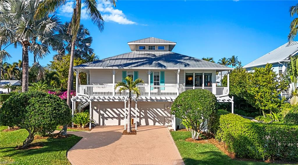 Raised beach house featuring decorative driveway, a standing seam roof, a garage, and a balcony