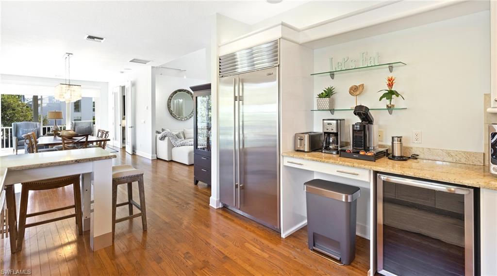 Kitchen featuring wine cooler, stainless steel built in fridge, light stone countertops, light wood-style floors, and suspended lighting