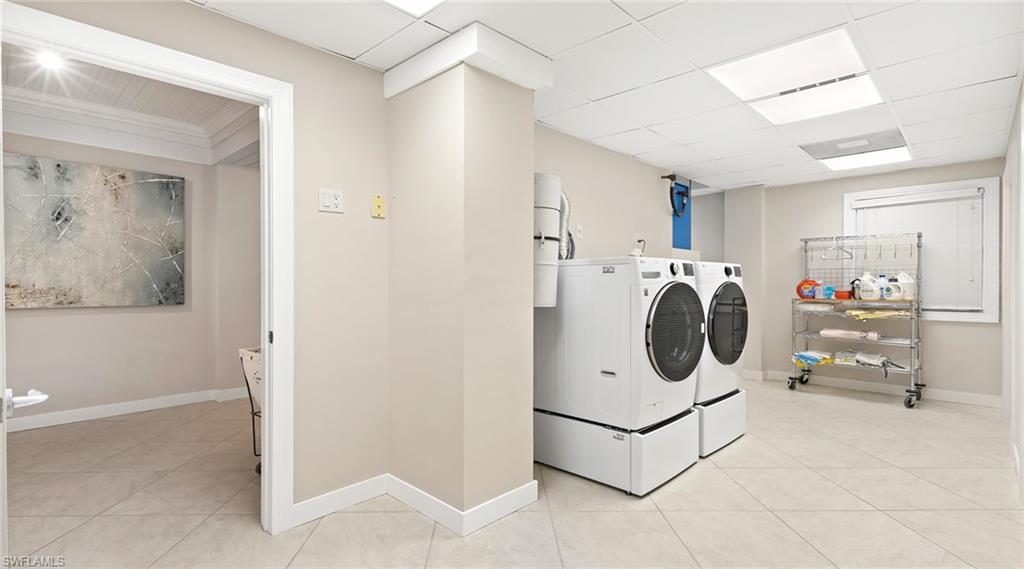 Laundry area featuring independent washer and dryer, light tile patterned floors, and a drop ceiling