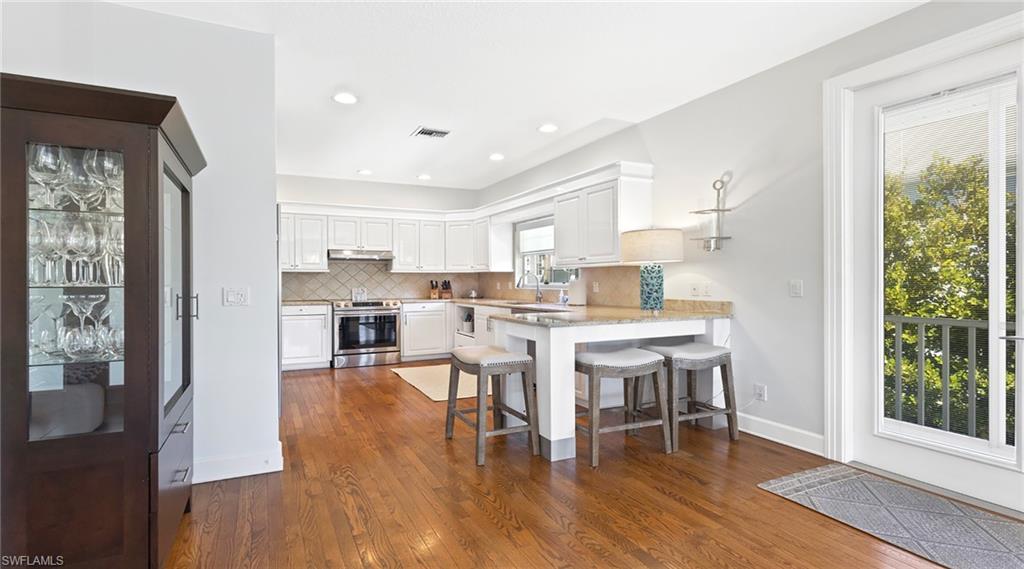 Kitchen with a breakfast bar, a peninsula, stainless steel electric range oven, decorative backsplash, and white cabinetry