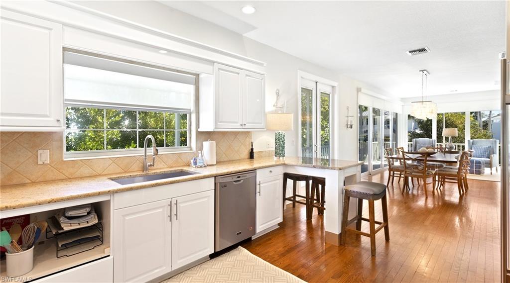 Kitchen featuring dark wood-style flooring, light stone countertops, a breakfast bar, dishwasher, and white cabinetry
