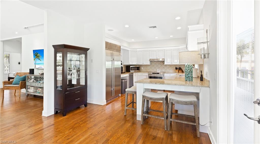 Kitchen with a kitchen breakfast bar, light stone counters, a peninsula, white cabinetry, and stainless steel appliances