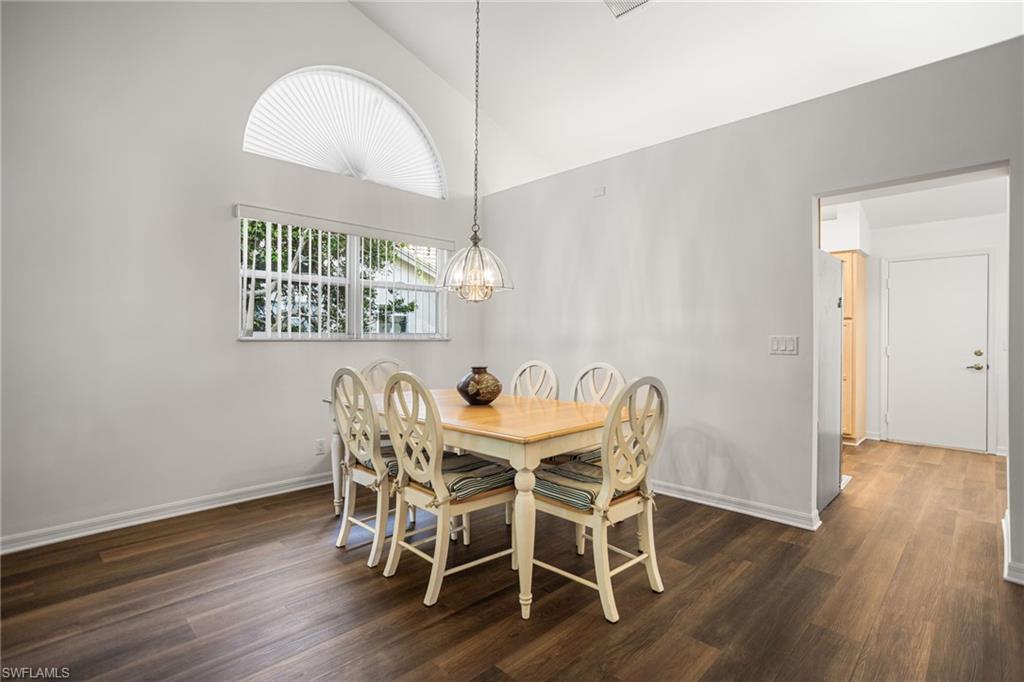 Elegant dining room featuring warm wood-finish flooring, a round dining table with seating for six, and a decorative pendant light fixture suspended from the vaulted ceiling.